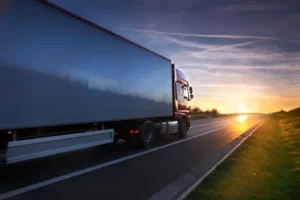 Ein Lkw fährt auf einer Straße in Richtung Sonnenuntergang.